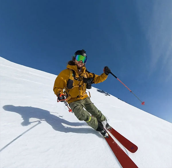 Skier in yellow jacket and green pants carving turns on a sunny snow-covered mountain slope