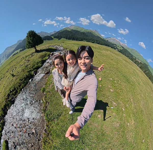 Happy family taking a wide-angle 360 selfie in a grassy mountain valley