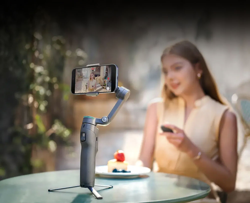 a woman sat at a table using the osmo mobile 8p to film herself wasting at a cafe