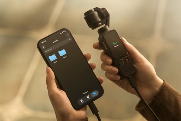 someone holding the dji osmo pocket 4 while it is connected to a smartphone via usb c