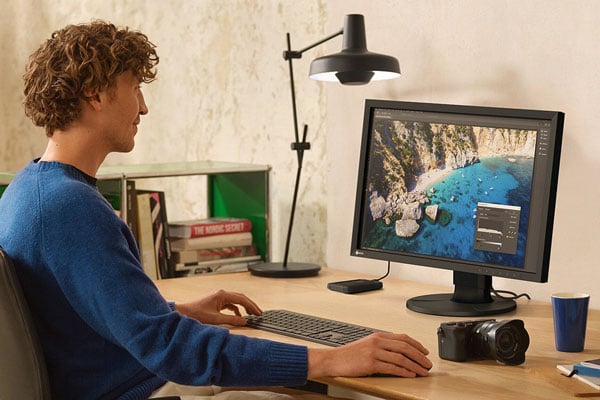 A photographer working on a colour-accurate EIZO ColorEdge monitor at a wooden desk setup