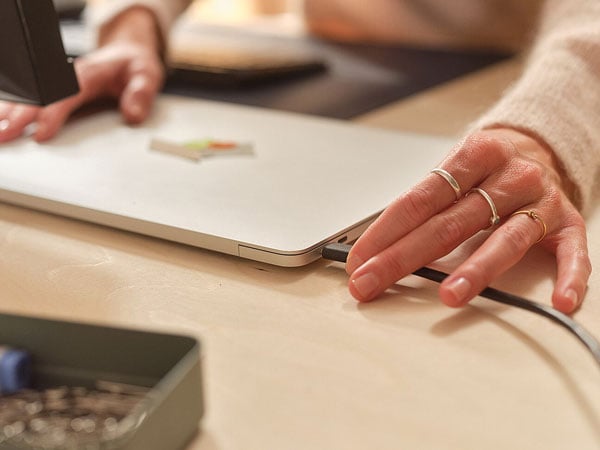 Person plugging a USB-C charging cable into a silver laptop on a desk