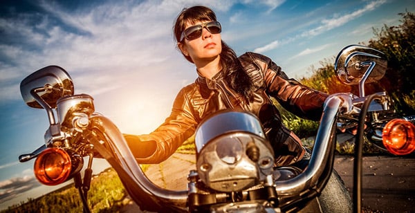 a woman wearing a brown leather jacket and sunglasses while seated on a motorcycle