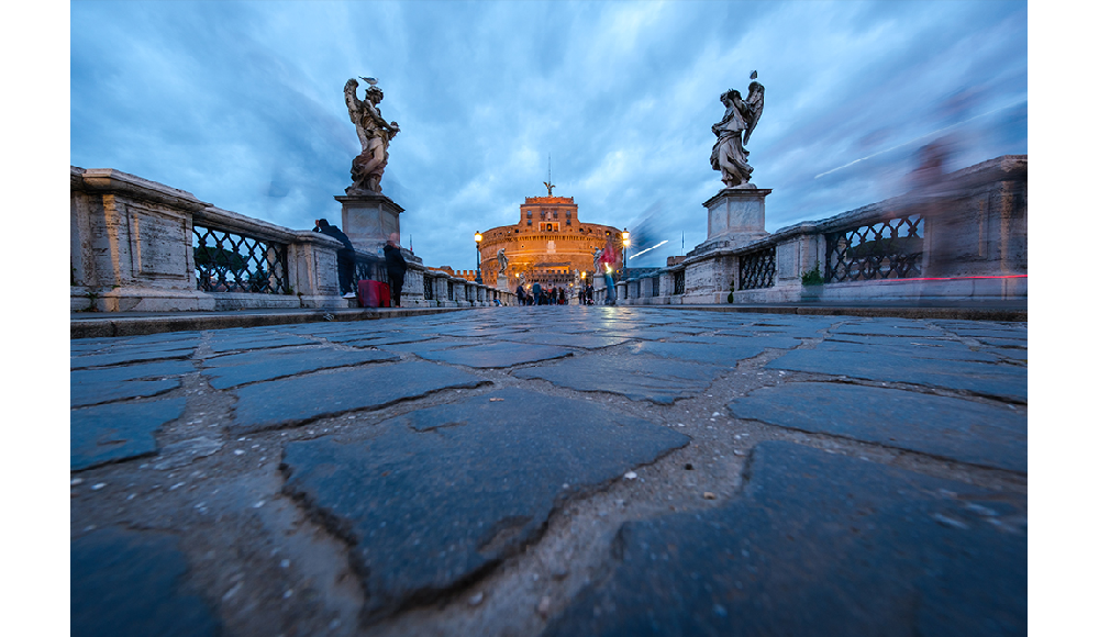 Fujifilm XF8mm F3.5 R WR sample image long exposure of people walking across a bridge with a fort in the background