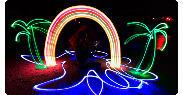 light painting of green palm trees and rainbow painted on beach at night