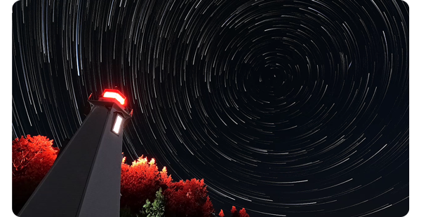 image of light house illuminated at night looking up at the night sky with circular star light trails