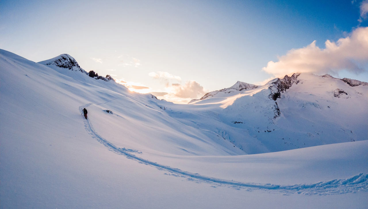 wide angle view of snow covered mountain peaks with two hikers walking across ridgeline