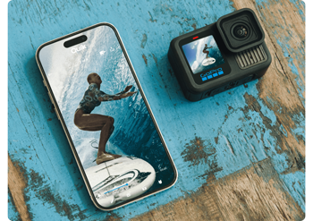 Apple iPhone and GoPro HERO13 Black sitting on distressed blue wooden table transferring footage of surfer riding waves