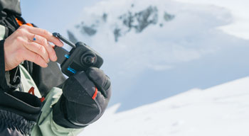 Person replacing battery in GoPro Hero Max2 camera while on snow covered mountains