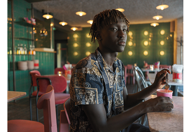 Hasselblad XCD 2.8/38V Lens Sample Image portrait of young black man sat eating with a spoon at a diner table with green tiled walls