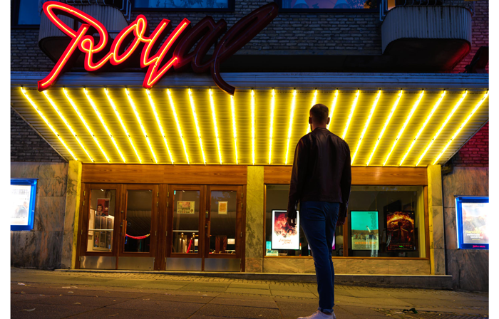 hasselblad X2D XCD 4/28P Sample image of a man stood looking at a movie theater with bright yellow neon lighting across the entrance veranda with a red neon sign that says Royal