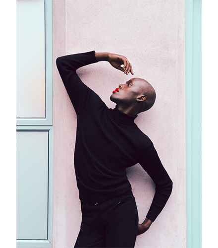 Hasselblad XCD 4/45P Lens sample image of bald black female model with bright red lipstick dressed in all black posing infront of a pastel pink and blue wall