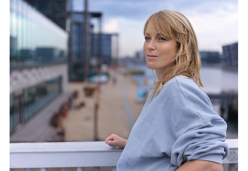 Hasselblad XCD 2.8/55v Lens Sample Image portrait of blonde woman wearing grey sweatshirt over looking a street from a pedestrian bridge