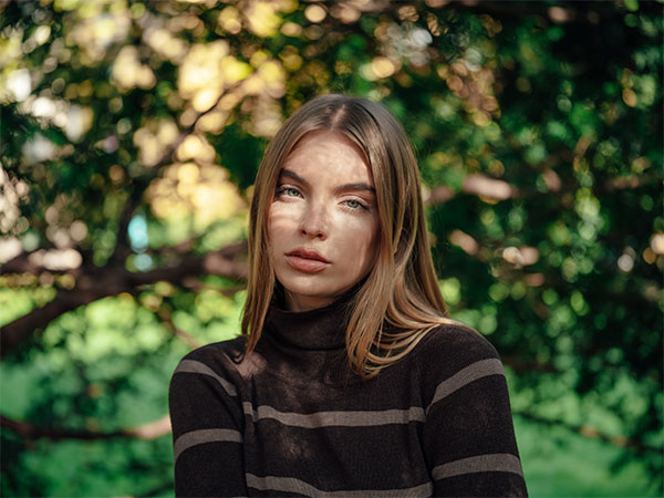 XCD 75P Lens sample portrait image of blonde female model wearing striped jumper sitting in front of trees in blurred bokeh