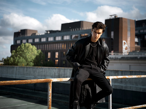 Hasselblad XCD 75P Sample image of male model wearing all black outfit sitting on rusted metal railing infront of large industrial building