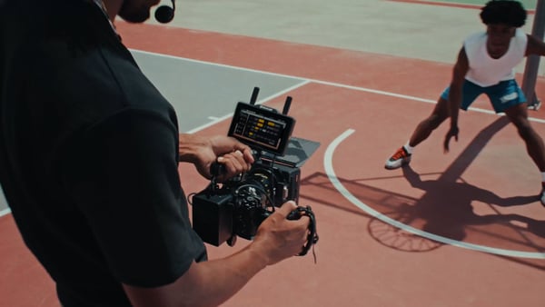someone filming a basketball player using the hollyland wireless monitor mounted to the top of a camera