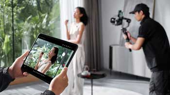 Director using apple iPad tablet to monitor video of model standing infront of window