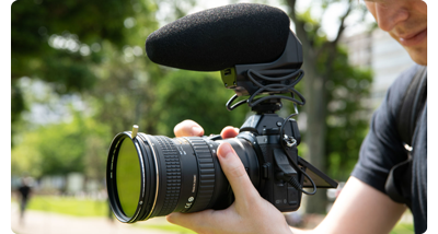 photograph of filmmaker holding mirrorless camera with HOYA VND lens filter and shotgun microphone