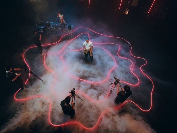 a man being filmed from 4 directions while stood in the middle of smoke and red lights