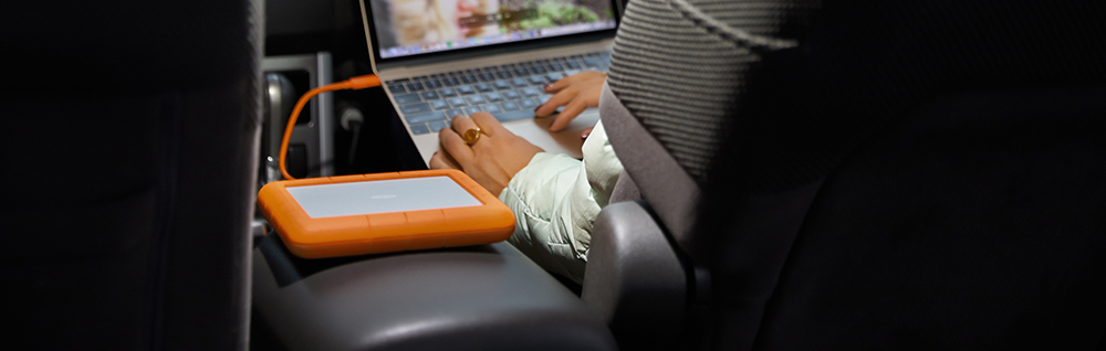 LaCie Rugged RAID drive on chair armrest with person working on macbook
