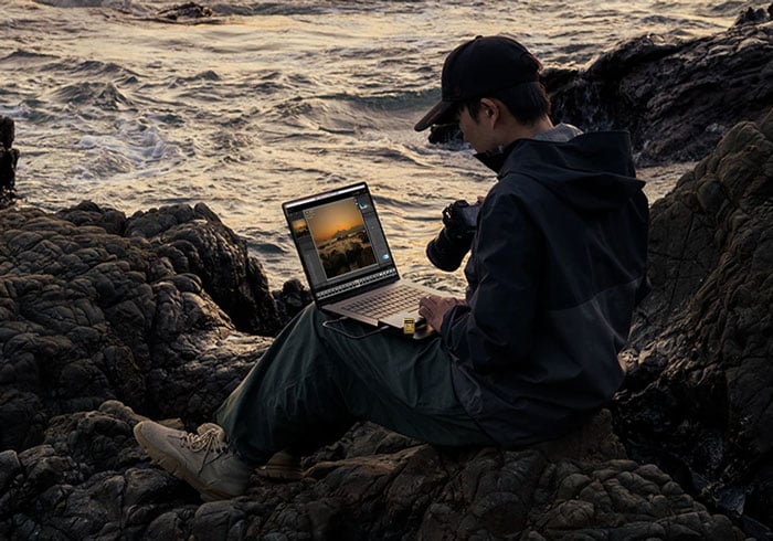 someone unloading the lexar armor gold sd card onto a laptop sat on rockss near the ocean