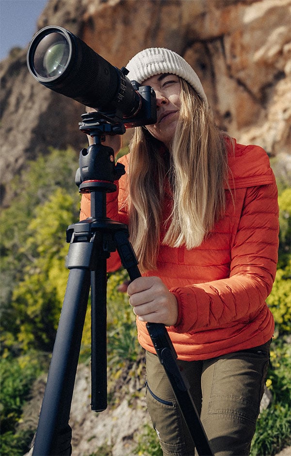 someone taking a photo near a cliffside using the manfrotto tripod and a camera with a telephoto lens