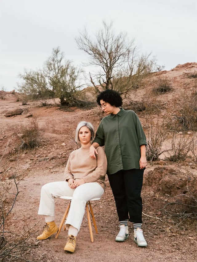 sample image of 2 people, one sat in a chair and the other standing, in the desert