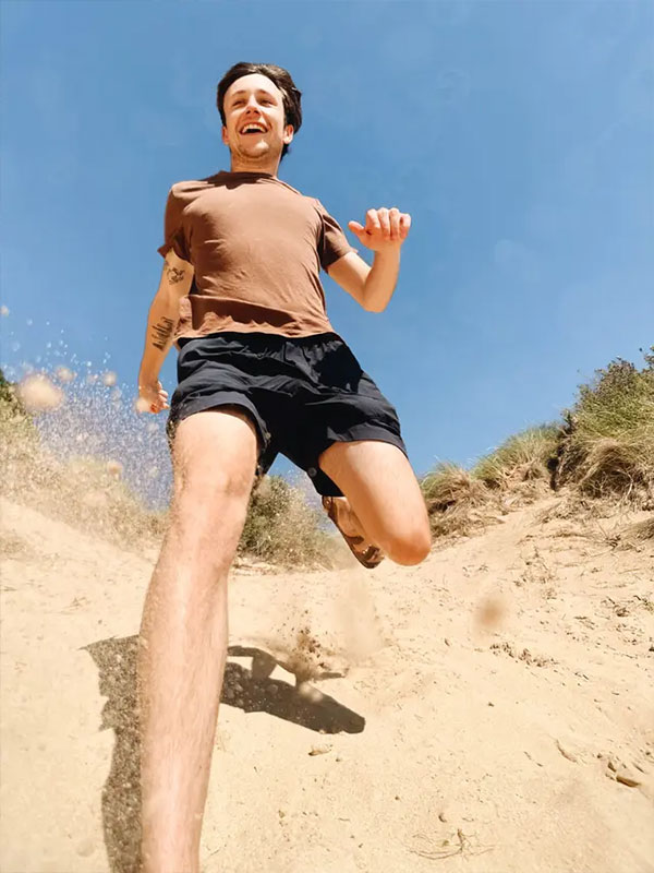 sample photo of a man running towards the camera on a beach taken using the moment mobile lens