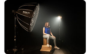 Image of black photography studio with model sat on wooden boxes with nanlite FS-150B with big softbox casting light on the model
