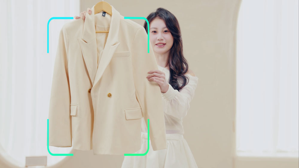 a woman holding up a cream coat that is being tracked by the obsbot ptz camera