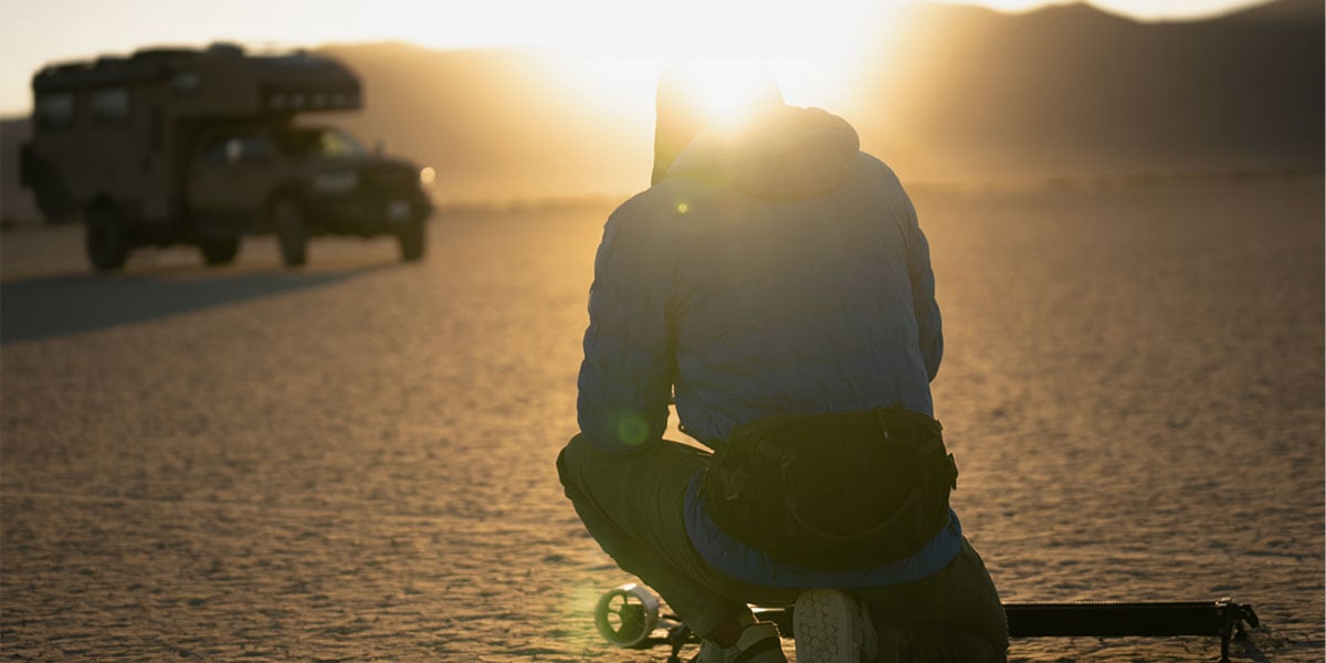 someone crouched down near a camper van in a desert