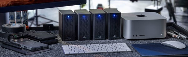 Four OWC Express 4M2 Ultra desktop RAID storage enclosures daisy-chained next to an Apple Mac Studio computer with a keyboard and mouse.