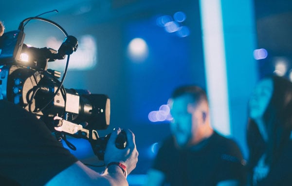 A professional video camera filming a man on a brightly lit blue studio stage