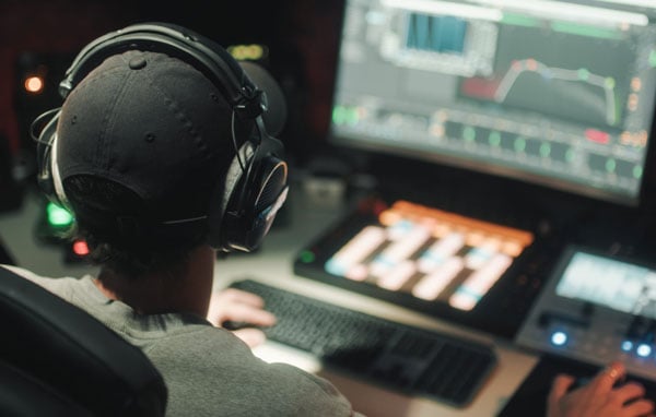 Audio engineer wearing headphones working at a sound mixing console and editing software in a production studio