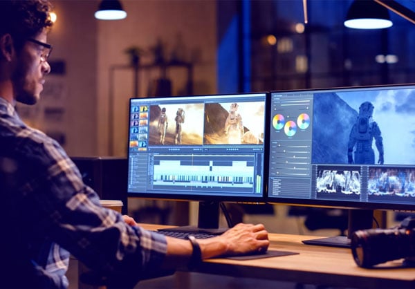 a man sat a wooden desk editing footage on two monitors