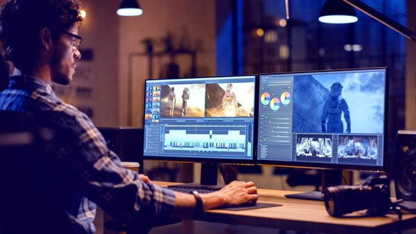 a man working at a desk with two monitors and a camera
