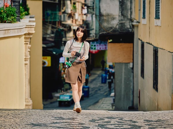 a woman walking down a cobblestone street in Macau holding the panasonic lumix l10 camera