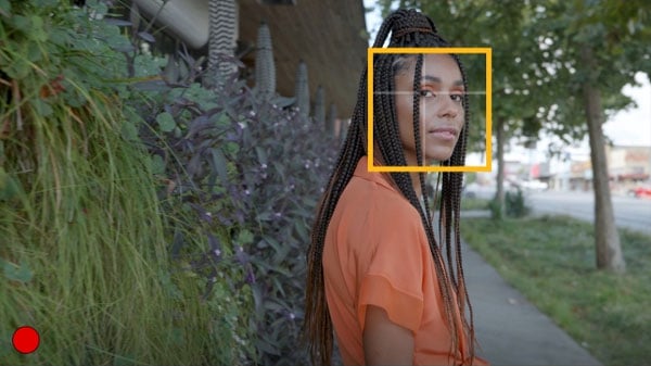 a person wearing a vibrant orange top with long, braided hair being recorded through the lumix s lens