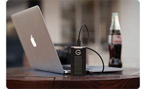 g drive ssd connected to a laptop on a table with a drink near by