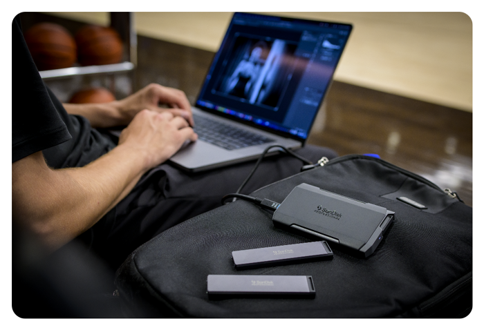 person working on macbook with SanDisk PRO-BLADE SSD sat on backpack next to them