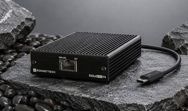 Front view of a black Sonnet Solo10G T5 bus-powered external network adapter on rocks showing the RJ45 port