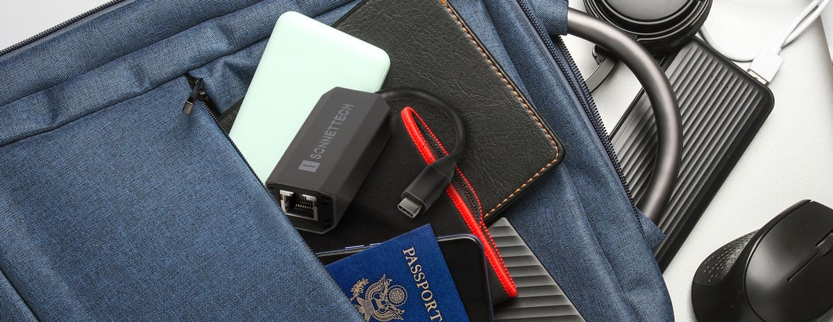 Sonnettech Ethernet adapter, passport, and tech accessories inside a blue backpack