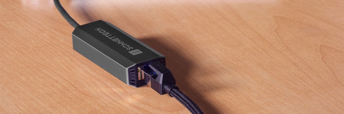 Sonnettech Thunderbolt to Ethernet adapter plugged into an RJ45 network cable on a wooden desk