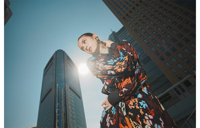 Sony a1 Mirrorless Camera sample Image of female model wearing bright flowery jacket standing between tall modern skycrapers with bright blue sky