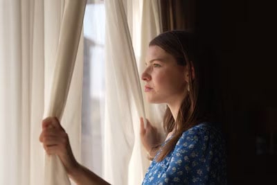sample image of a woman looking through a window while holding the curtains open