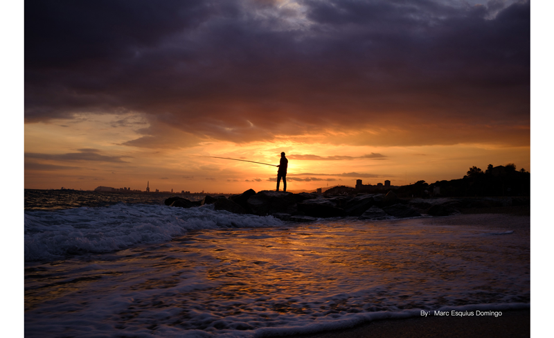 sample photograph of man fishing on rocks outcrop on a beach lit by sunset