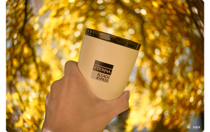 sample photograph person holding cup in front of trees covered with yellow leaves