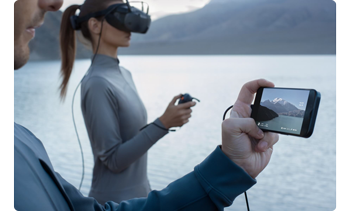 person holding smartphone connected to pilot wearing DJI Goggles N3 standing infront of lake