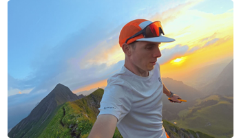 image of male runner wearing orange cap running across mountain top at sunset