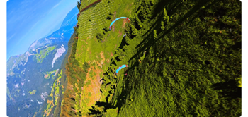 video still frame of two paragliders flying above vibrant green fields in mountain range